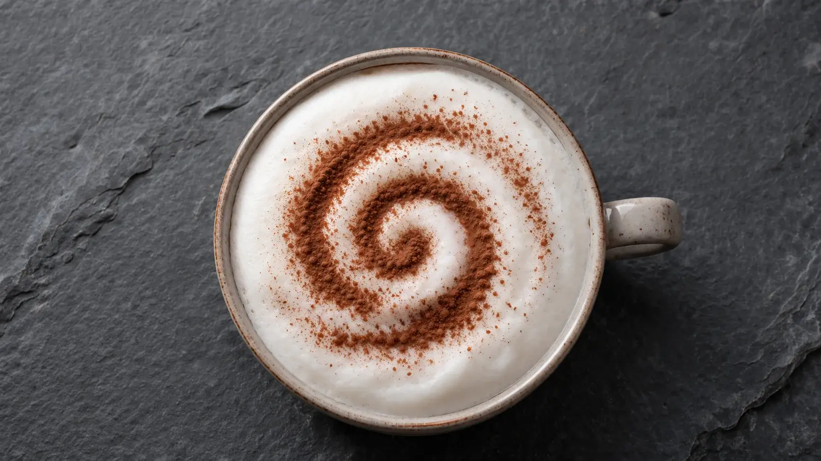 Vue de dessus d'une tasse de cappuccino protéiné mousseux, mousse de lait dense avec motif en forme de cœur tracé au cacao, sur une ardoise grise