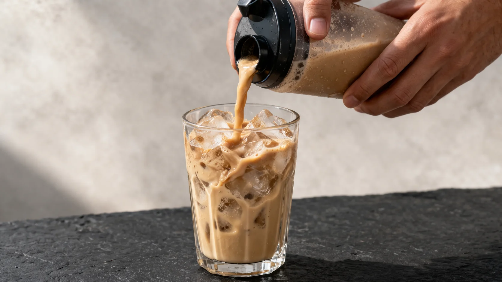 Versement du café protéiné glacé dans un grand verre rempli de glaçons, mouvement visible