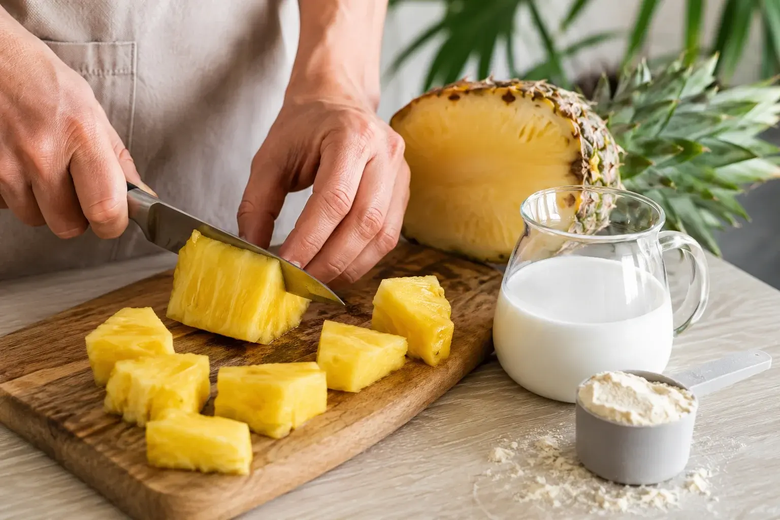 Morceaux d'ananas frais découpés sur une planche à côté d'un verre doseur de lait de coco