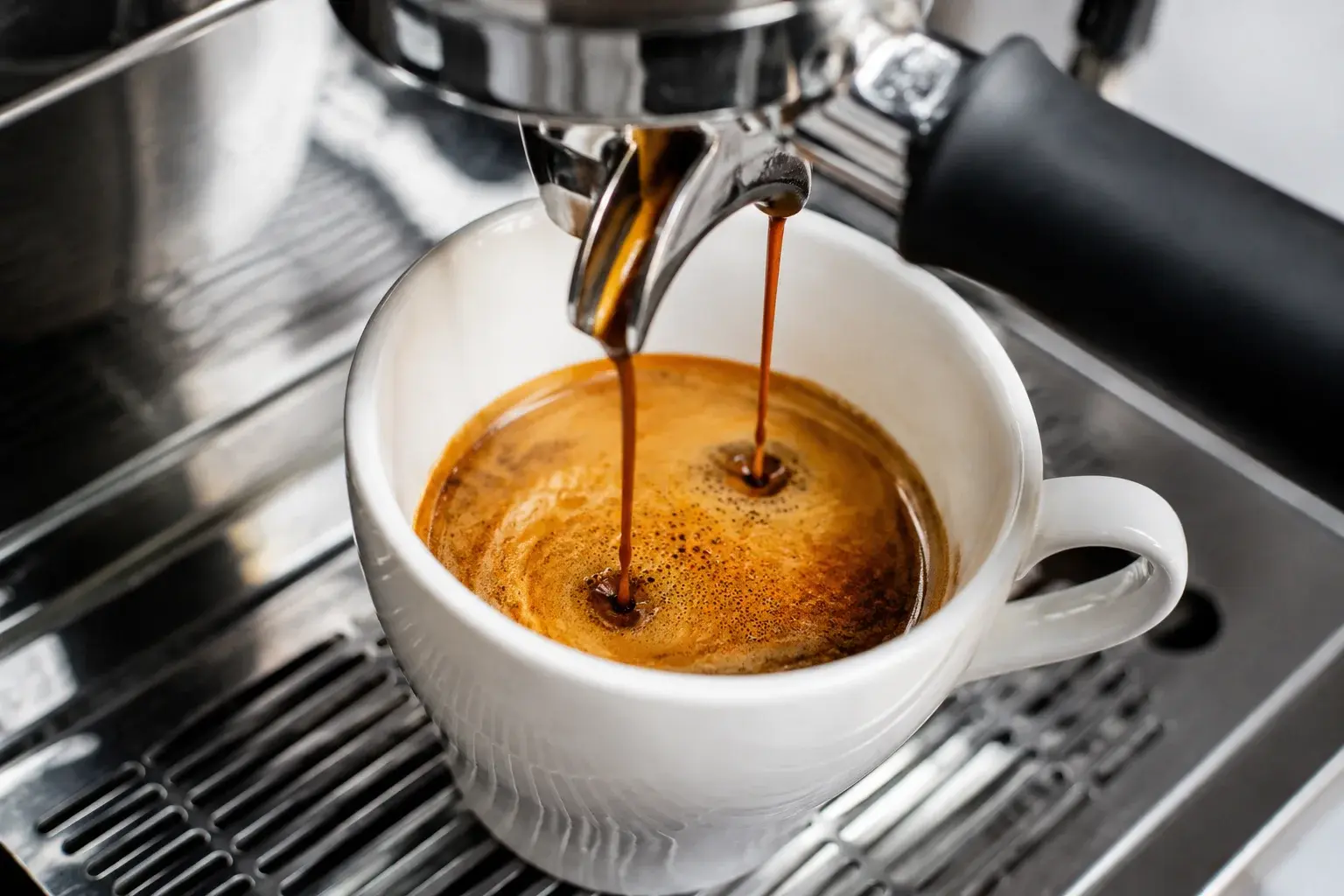 Double espresso noir qui coule depuis une machine à café professionnelle dans une tasse blanche en céramique, crema dorée se formant