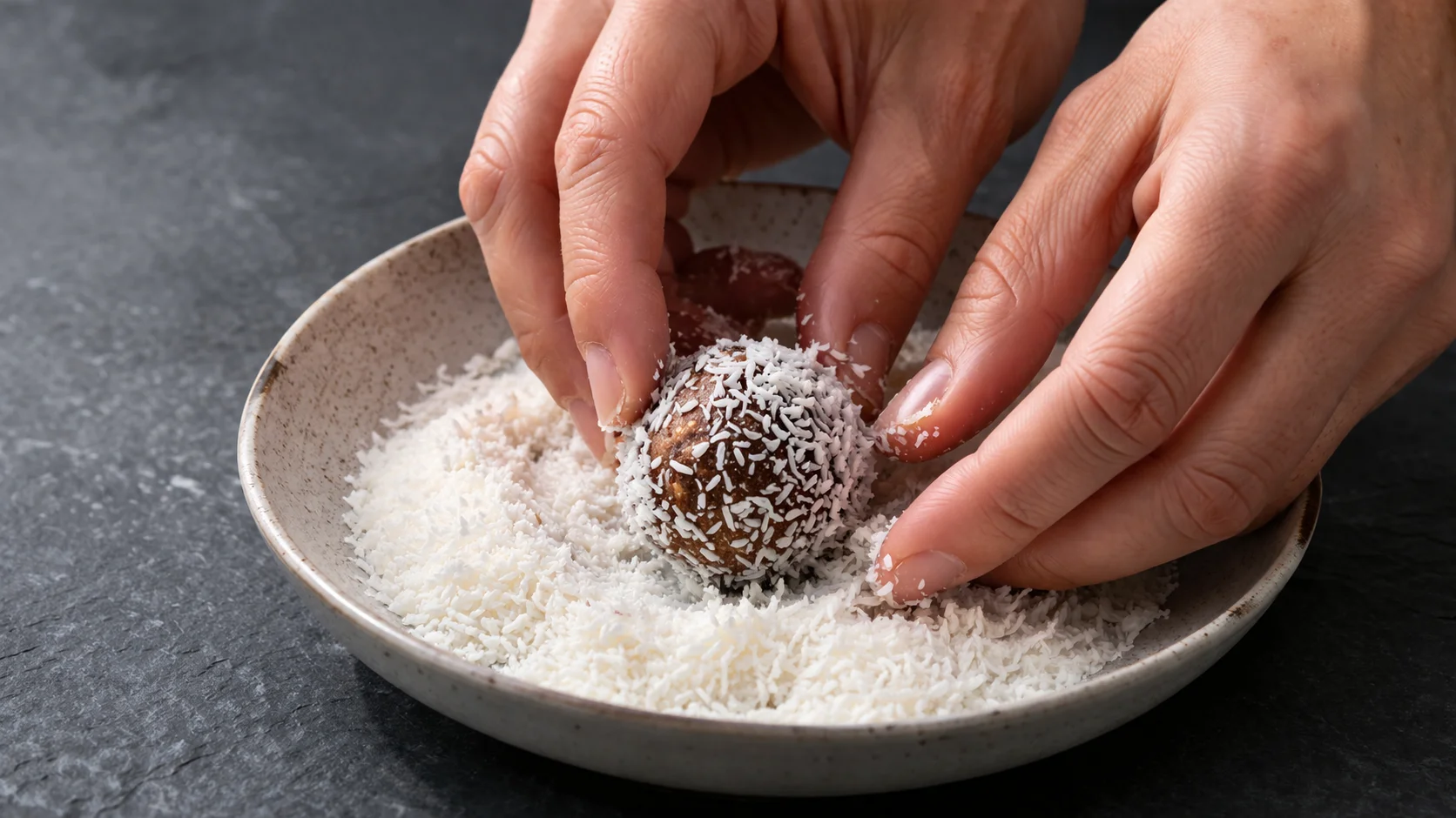 Roulage des protein balls dans l'assiette de noix de coco râpée pour l'enrobage final