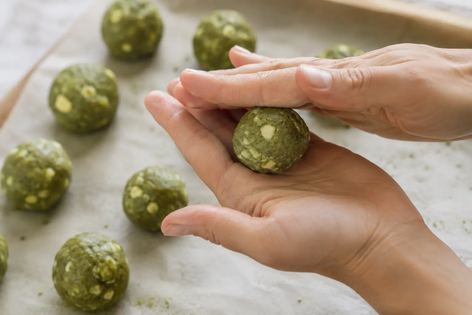 Mains roulant une boule de pâte verte au matcha entre les paumes