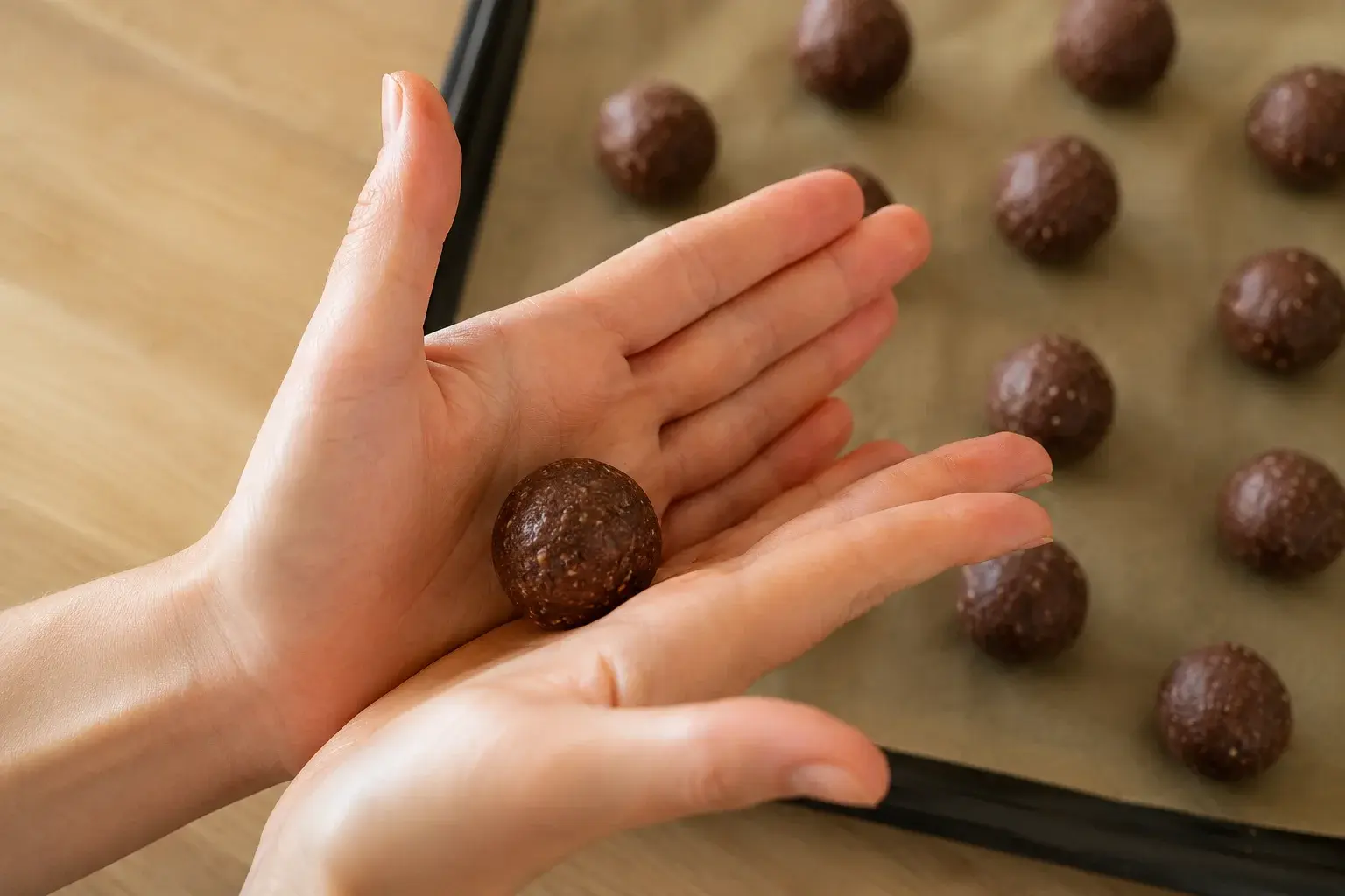 Mains qui roulent une boule de pâte chocolat-noisette entre les paumes, autres balls déjà formées disposées sur une plaque en arrière-plan