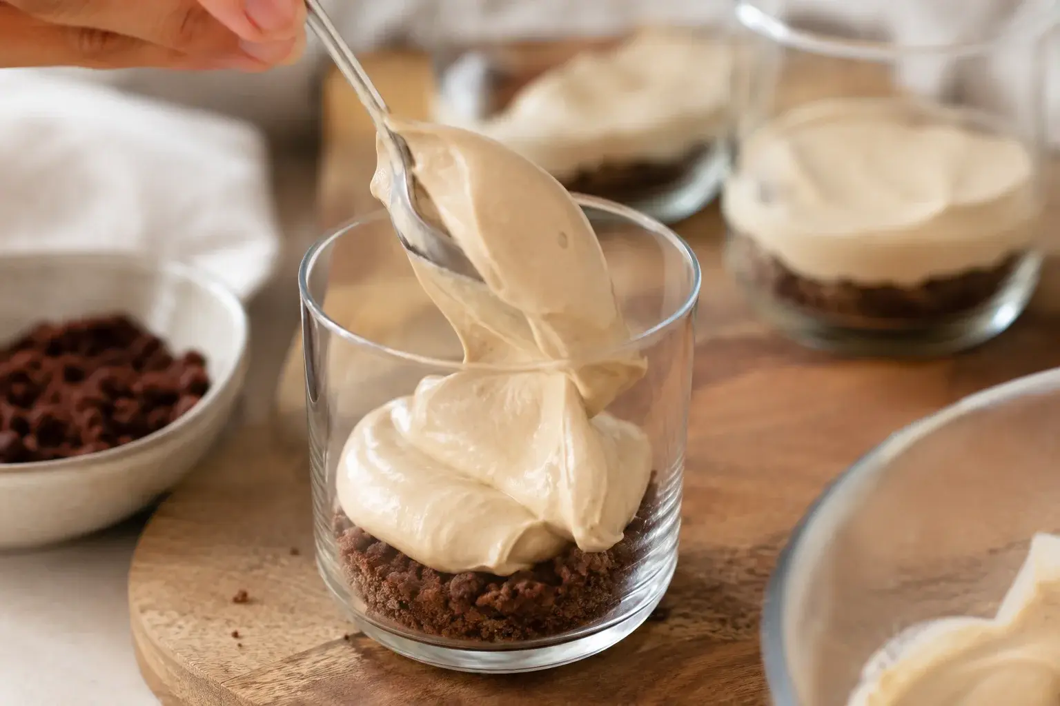 Cuillère déposant la crème au café dans une verrine sur une couche de crumble cacao