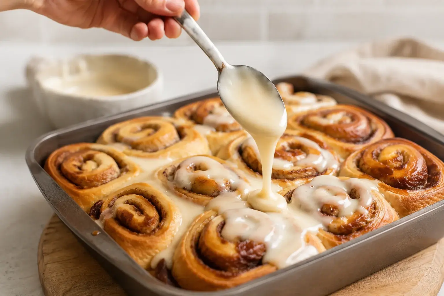 Main versant un glaçage blanc crémeux à la cuillère sur des cinnamon rolls dorés