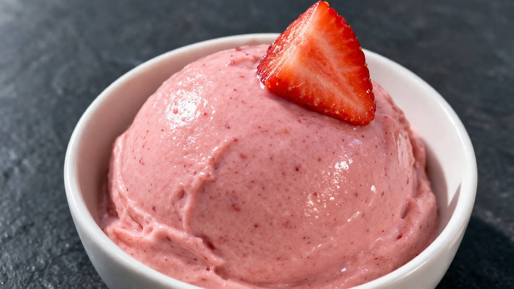 Gros plan sur une boule de nice cream fraise rose et onctueuse dans un bol blanc, texture crémeuse et lisse avec un éclat de fraise fraîche sur le dessus
