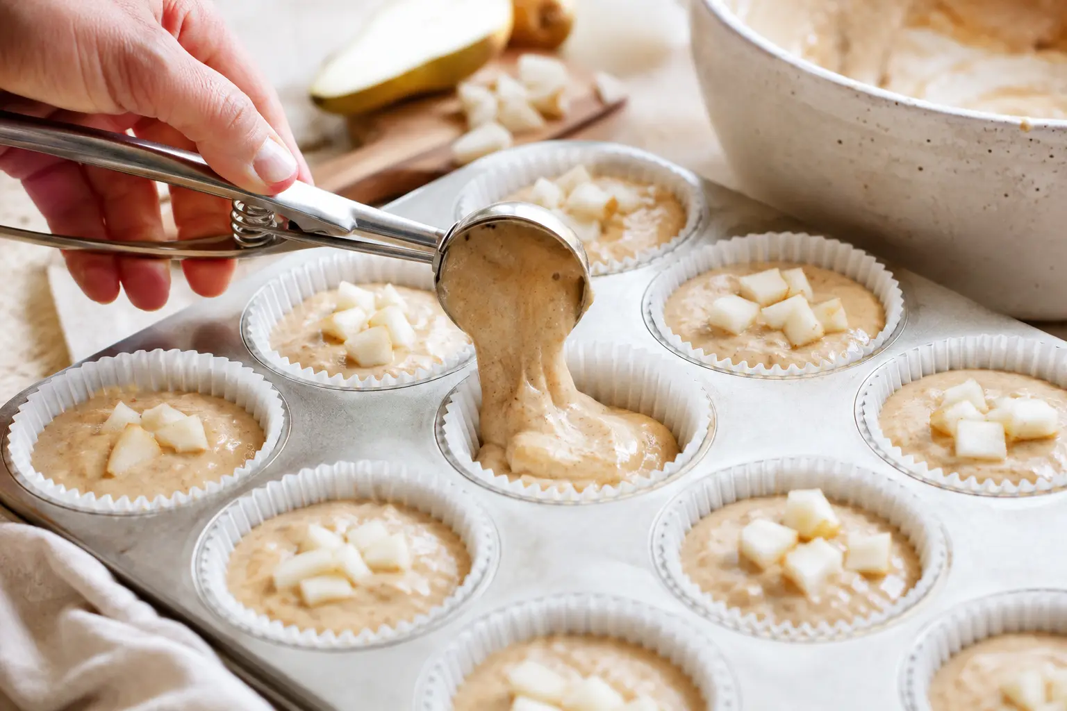 Pâte à muffins versée à la cuillère dans des caissettes en papier avec des morceaux de poire sur le dessus