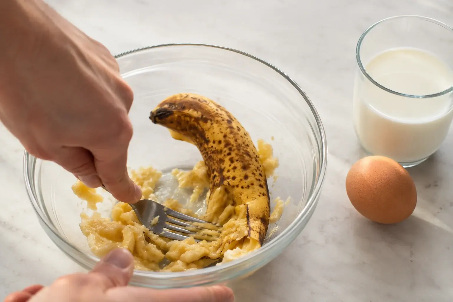 Main écrasant une banane mûre à la fourchette dans un saladier en verre