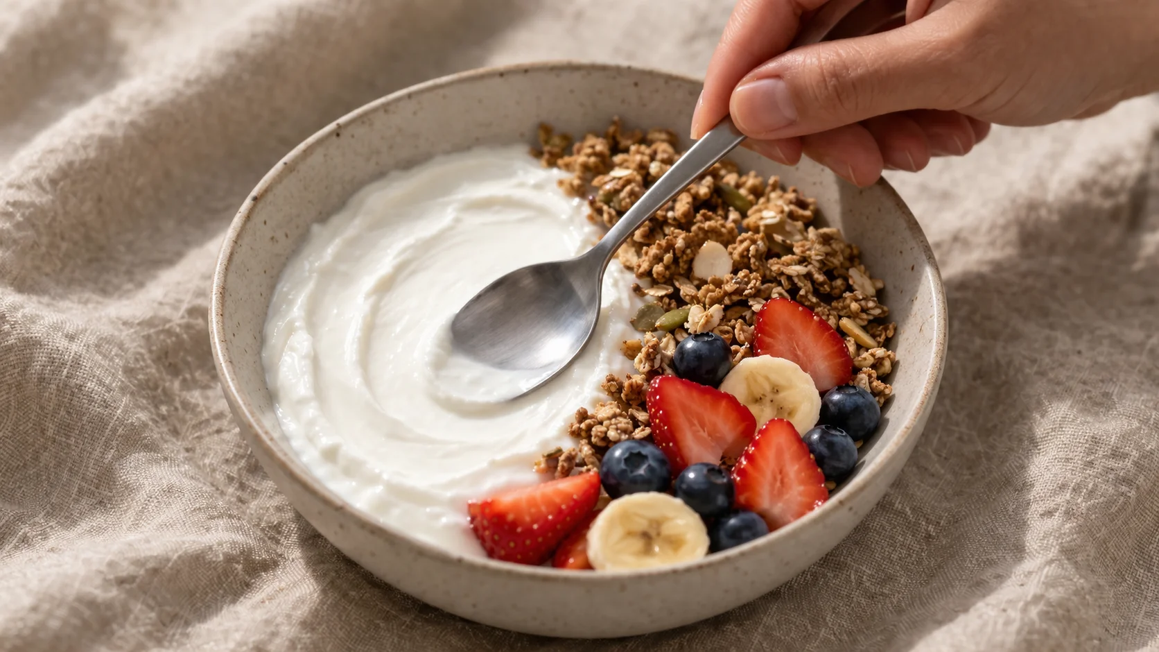 Bowl en cours de montage avec fromage blanc lissé, granola déposé sur un côté et fruits frais disposés en sections colorées