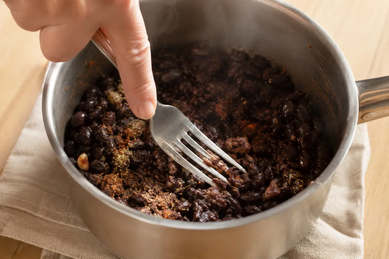 Haricots noirs écrasés à la fourchette dans une casserole avec épices