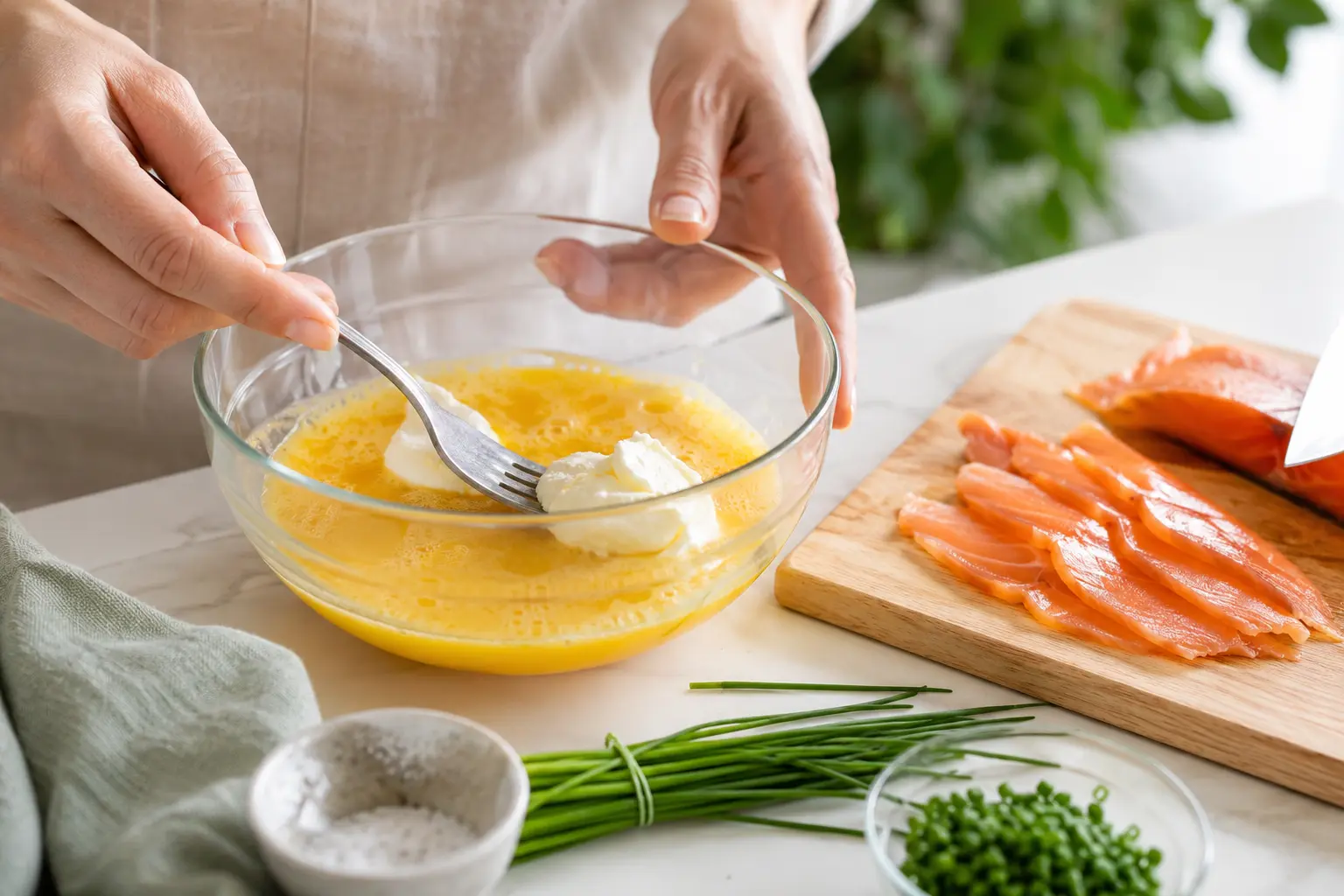 Œufs battus dans un bol avec fromage frais, à côté de tranches de saumon fumé découpées