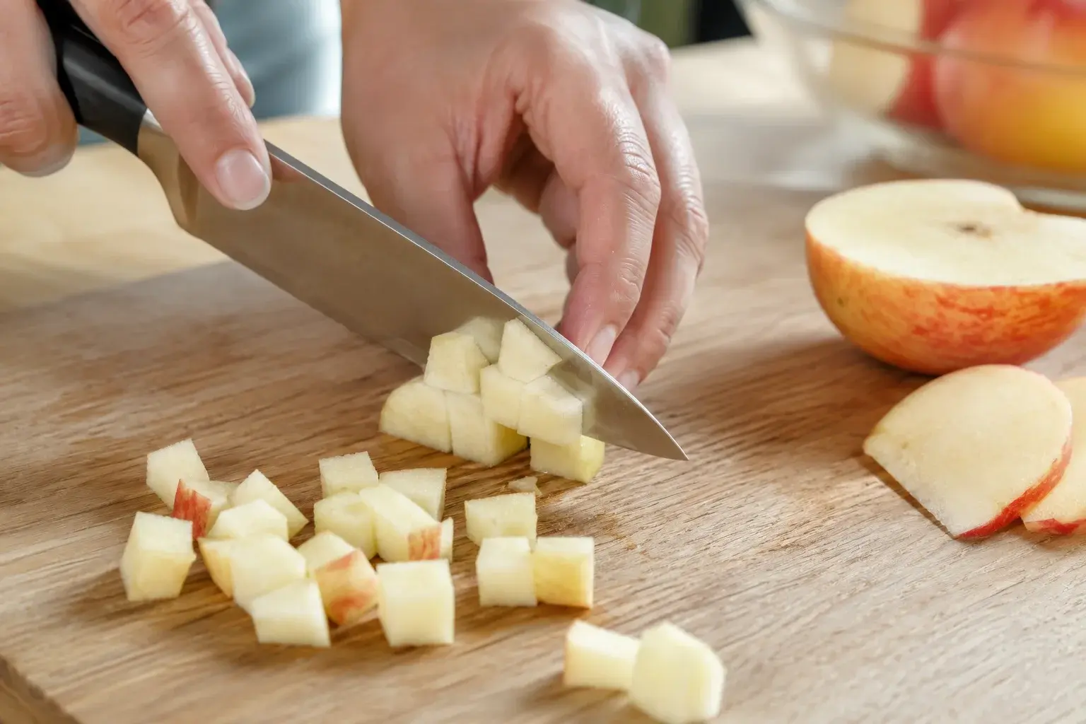 Main coupant une pomme en petits dés sur une planche à découper en bois