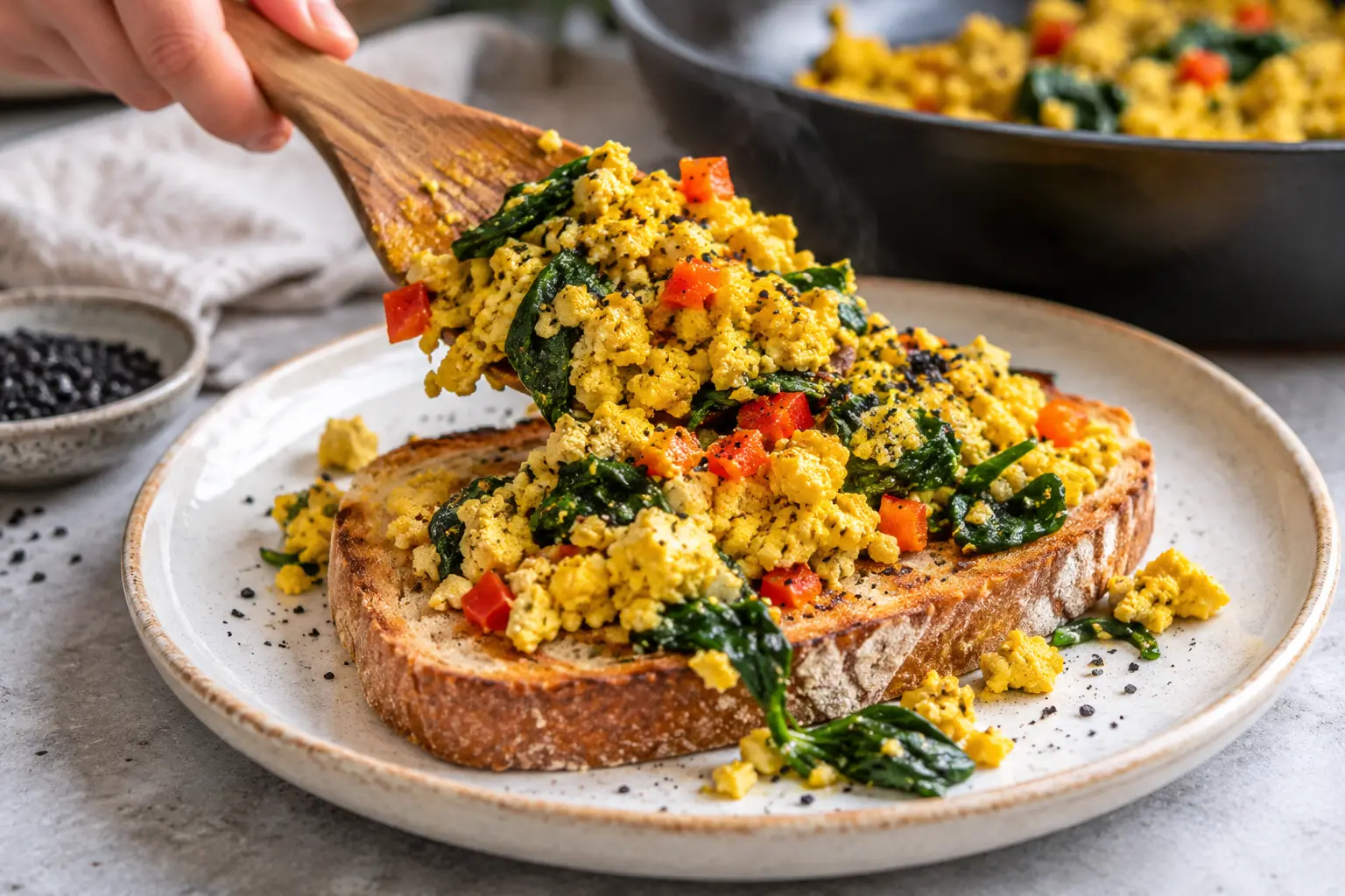 Tofu brouillé doré servi sur du pain grillé avec des épinards tombés