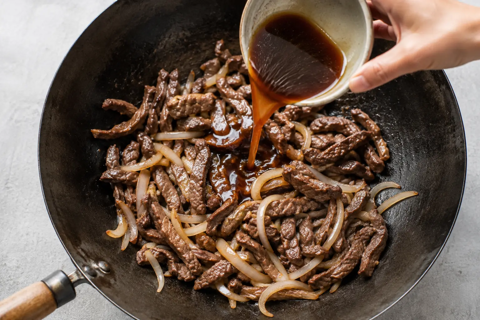 Bœuf remis dans le wok avec les oignons et la sauce en train de caraméliser