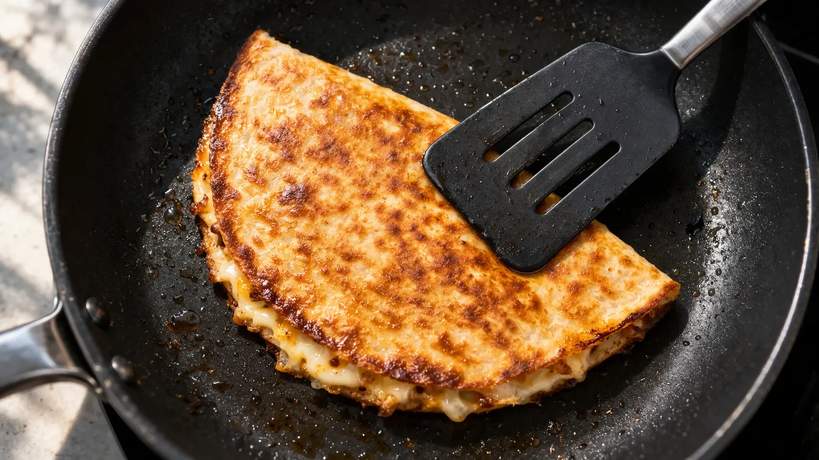 Quesadilla en train de dorer dans une poêle antiadhésive, vue de dessus, avec une spatule qui appuie dessus