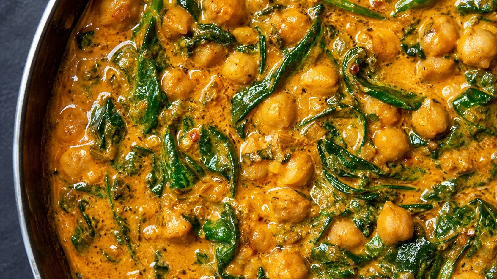 Gros plan sur la texture crémeuse du curry de pois chiches aux épinards avec pois chiches entiers et feuilles d'épinards dans la sauce orange