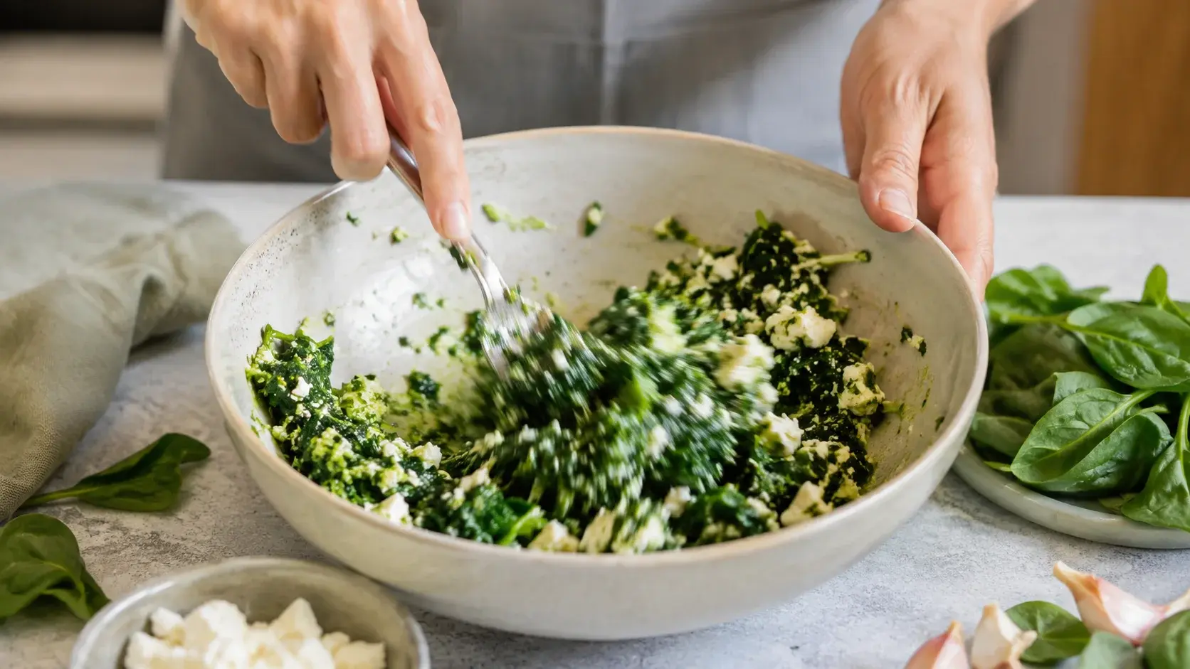 Mains qui mélangent une farce verte aux épinards et morceaux de feta blanche dans un saladier en céramique