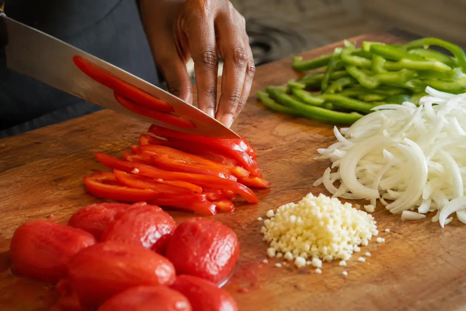 Planche en bois avec lamelles de poivrons rouges et verts, oignon émincé, ail haché et tomates pelées concassées