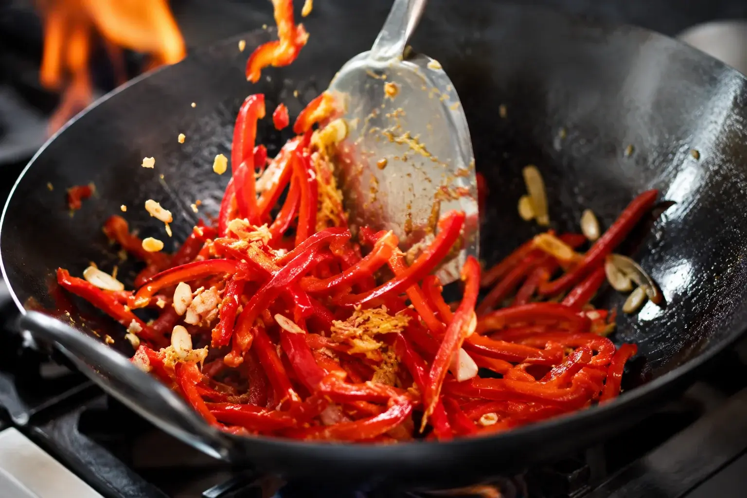 Poivron rouge, ail et gingembre en train de sauter dans un wok à feu vif