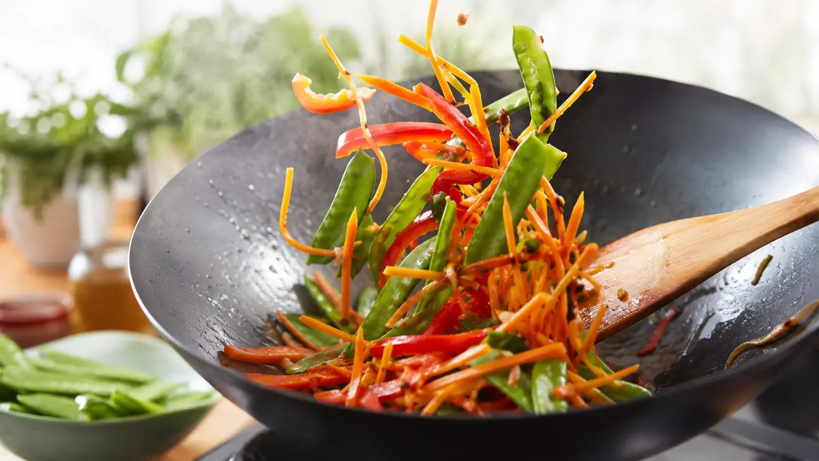 Légumes colorés sautés dans un wok, julienne de carottes, lamelles de poivron rouge et pois gourmands verts en mouvement