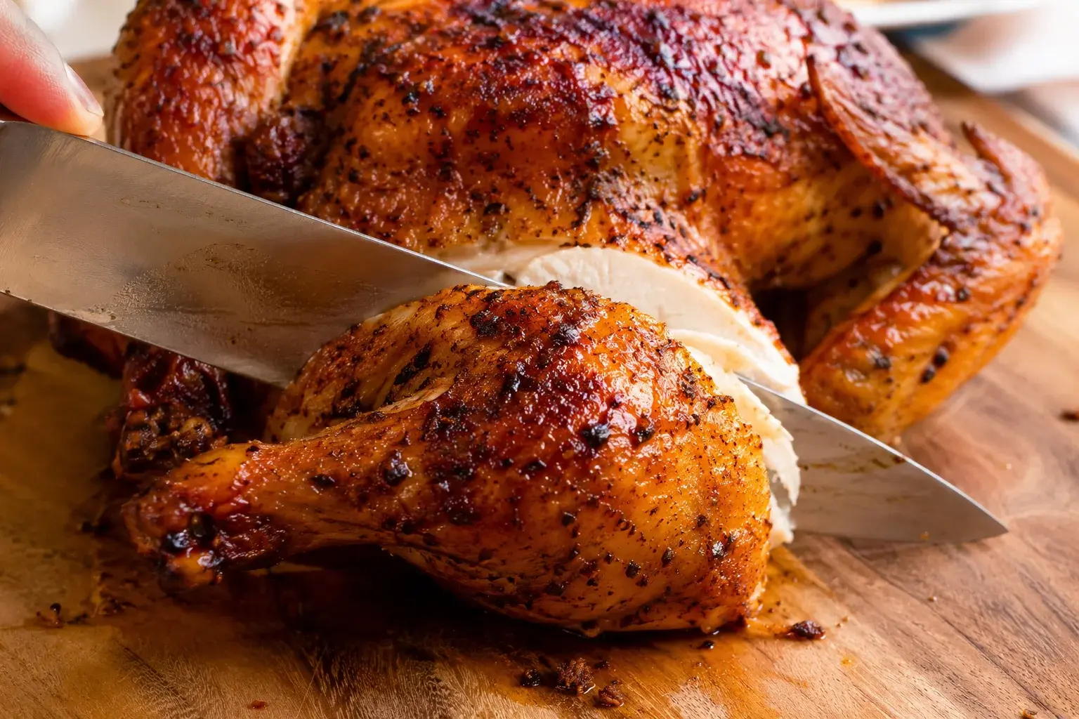 Couteau qui découpe une cuisse d'un poulet rôti aux épices cajun sur une planche en bois, chair blanche juteuse visible