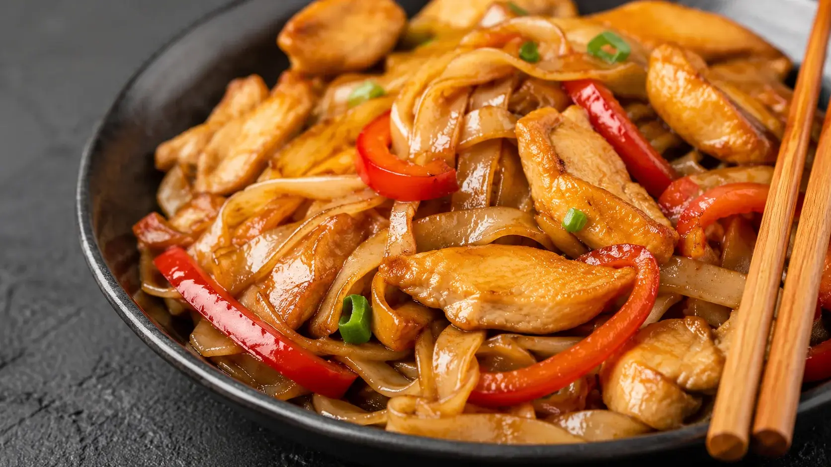 Gros plan sur des nouilles de riz enrobées de sauce soja brillante avec lanières de poulet doré et morceaux de poivron rouge